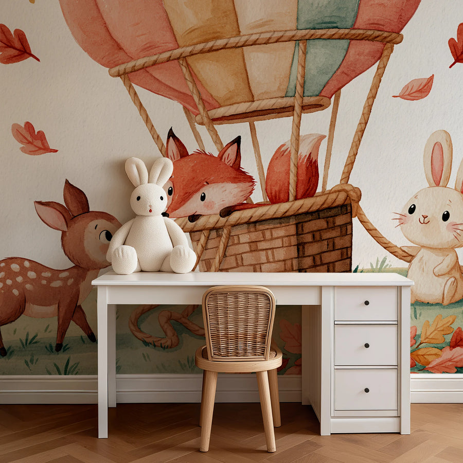 Woodland nursery wall mural with a hot air balloon and forest animals behind a white desk and rattan chair